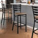Three Lancaster Table & Seating black finish ladder back bar stools with vintage wood seats at a counter.