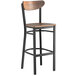 A Lancaster Table & Seating black bar stool with a vintage wood seat and back.