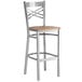 A Lancaster Table & Seating metal cross back bar stool with a wooden seat.