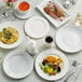 A table set with Tuxton bright white coupe china plates, bowls, and cups of food.