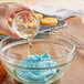 A person pouring LorAnn Preserve-It Antioxidant into blue frosting in a glass bowl.