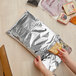 A hand holding a block of cheese in a foil package.
