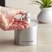 A person pouring liquid into an American Metalcraft stainless steel hand sanitizer dispenser.