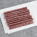 A pile of thin red raw meat sticks on a white surface.