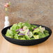 A CAC Festiware black bowl filled with salad on a table.
