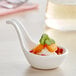 A close up of a white Tablecraft mini melamine tasting spoon filled with food.