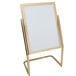 An Aarco brass double pedestal poster stand with a white board on it.