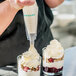A person pouring Rich's On Top whipped dessert topping into a clear cup of dessert.