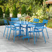 A blue Lancaster Table & Seating outdoor dining table with blue chairs on a concrete patio.