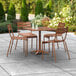 A Lancaster Table & Seating brown aluminum dining table with an umbrella hole and four chairs on an outdoor patio.