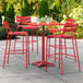 A red Lancaster Table & Seating bar height table with 4 chairs on a patio.
