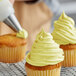 A person decorating a cupcake with Rich's Bettercreme yellow whipped icing using a pastry bag with a metal tip.