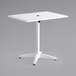 A white Lancaster Table & Seating outdoor table with a white powder-coated aluminum base and umbrella hole.