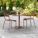 A Lancaster Table & Seating brown powder-coated aluminum table with two chairs on a patio.
