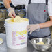 A woman mixing Rich's Bettercreme Lemon Whipped Icing in a white bucket.