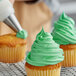 A person using a pastry bag and metal tip to decorate a cupcake with Rich's Bettercreme Green Whipped Icing.