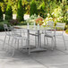 A Lancaster Table & Seating outdoor dining table with 4 chairs on a concrete patio with a white umbrella.