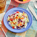 A plate of coleslaw with shredded cabbage and carrots on a purple Acopa melamine plate.