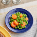 A blue Acopa Foundations melamine plate with a carrot and peas on it.