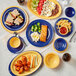 A table with Acopa blue melamine plates of food including chicken wings and vegetables and broccoli.