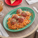 A green Acopa melamine oval platter with spaghetti and meatballs on a table.