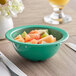 A green Acopa Foundations melamine bowl filled with fruit on a table.