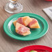 A piece of food wrapped in ham on a green Acopa Foundations melamine plate.
