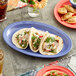 An Acopa purple narrow rim melamine oval platter with tacos and food on a table.
