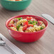 A red Acopa Foundations melamine bowl filled with pasta, tomatoes, and spinach on a napkin with a fork.