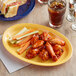 An Acopa yellow melamine oval platter with chicken wings, carrots, and celery on a table.