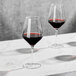 Two Della Luce Astro wine glasses filled with red wine on a marble table.