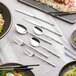 Acopa stainless steel bouillon spoons on a table with plates of food.