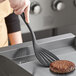 A person using a Tablecraft black silicone-coated stainless steel spatula to flip a burger.