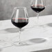 Two Della Luce Maia burgundy wine glasses filled with red wine on a marble table.