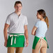 A man and woman wearing Choice Kelly Green poly-cotton waist aprons with natural webbing.