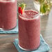 A glass of red Pitaya Foods acai berry smoothie with a straw and a strawberry on top.