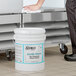 A person cleaning a school freezer shelf with a white bucket of Noble Chemical Arctic Kleen.