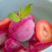 A bowl of pink Pitaya Foods sorbet with green leaves on top.
