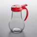 A Vollrath glass syrup dispenser with a red lid.