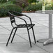 A Lancaster Table & Seating black outdoor arm chair on a concrete patio next to a table.