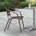 A brown Lancaster Table & Seating outdoor arm chair on a concrete patio next to a table with a glass of water.
