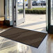 A brown Lavex Needle Rib indoor entrance mat in front of a large glass door.
