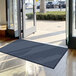 A blue Lavex Needle Rib entrance mat in front of a large glass door.