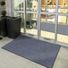 A large blue Lavex Plush Dilour entrance mat with a tree growing in a pot placed in front of a building's glass door.