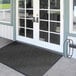A charcoal Lavex entrance mat with a black chevron pattern on a white door.