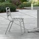 A Lancaster Table & Seating silver metal chair on a sidewalk.