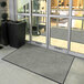 A large gray Lavex Plush Dilour carpeted entrance mat in front of a glass door.