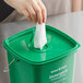 A hand pulling a tissue out of a green Noble Products King-Pail lid.