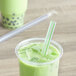 A Choice multicolor striped pointed boba straw in a green drink in a plastic cup.