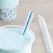 A cup of blue liquid with a Choice multicolor striped straw in it.